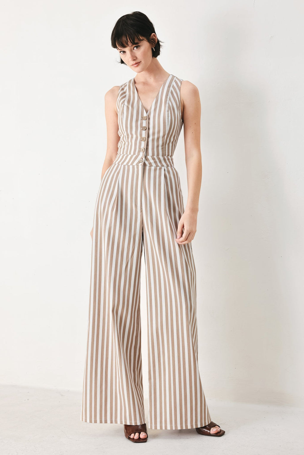 Natural Rhythm Woven Jumpsuit in Taupe White with stripe print, V-neckline, sleeveless cut, front button closure, and wide leg shown on model