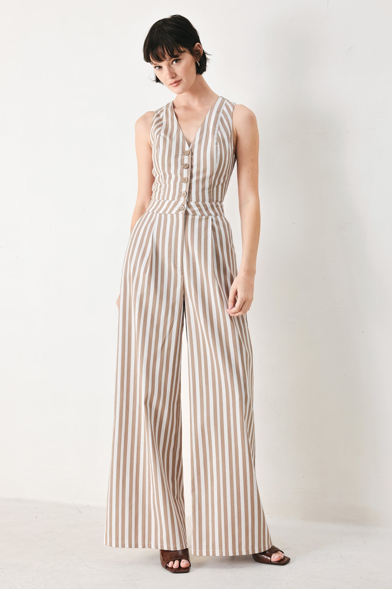 Natural Rhythm Woven Jumpsuit in Taupe White with stripe print, V-neckline, sleeveless cut, front button closure, and wide leg shown on model