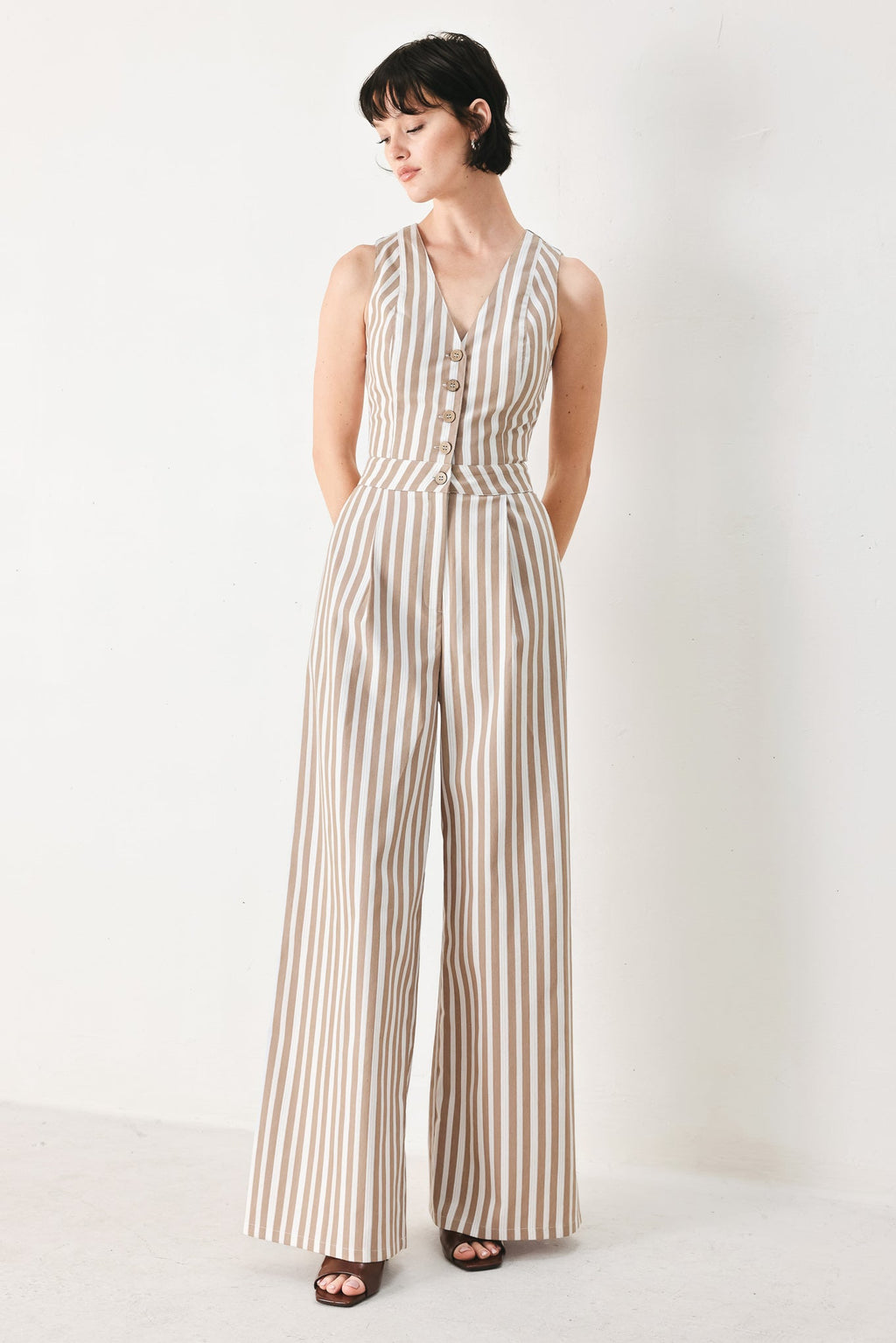 Natural Rhythm Woven Jumpsuit in Taupe White with stripe print, V-neckline, sleeveless cut, front button closure, and wide leg shown on model