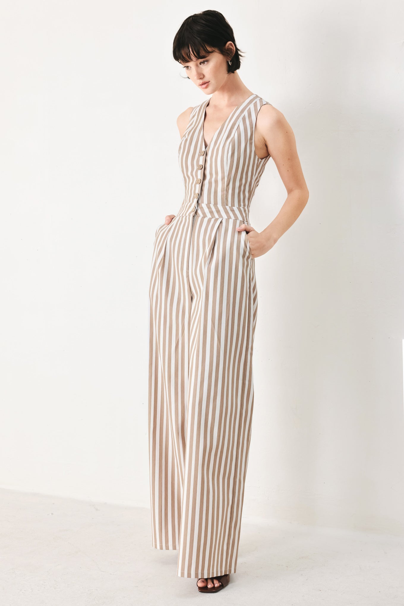 Natural Rhythm Woven Jumpsuit in Taupe White with stripe print, V-neckline, sleeveless cut, front button closure, and wide leg shown on model