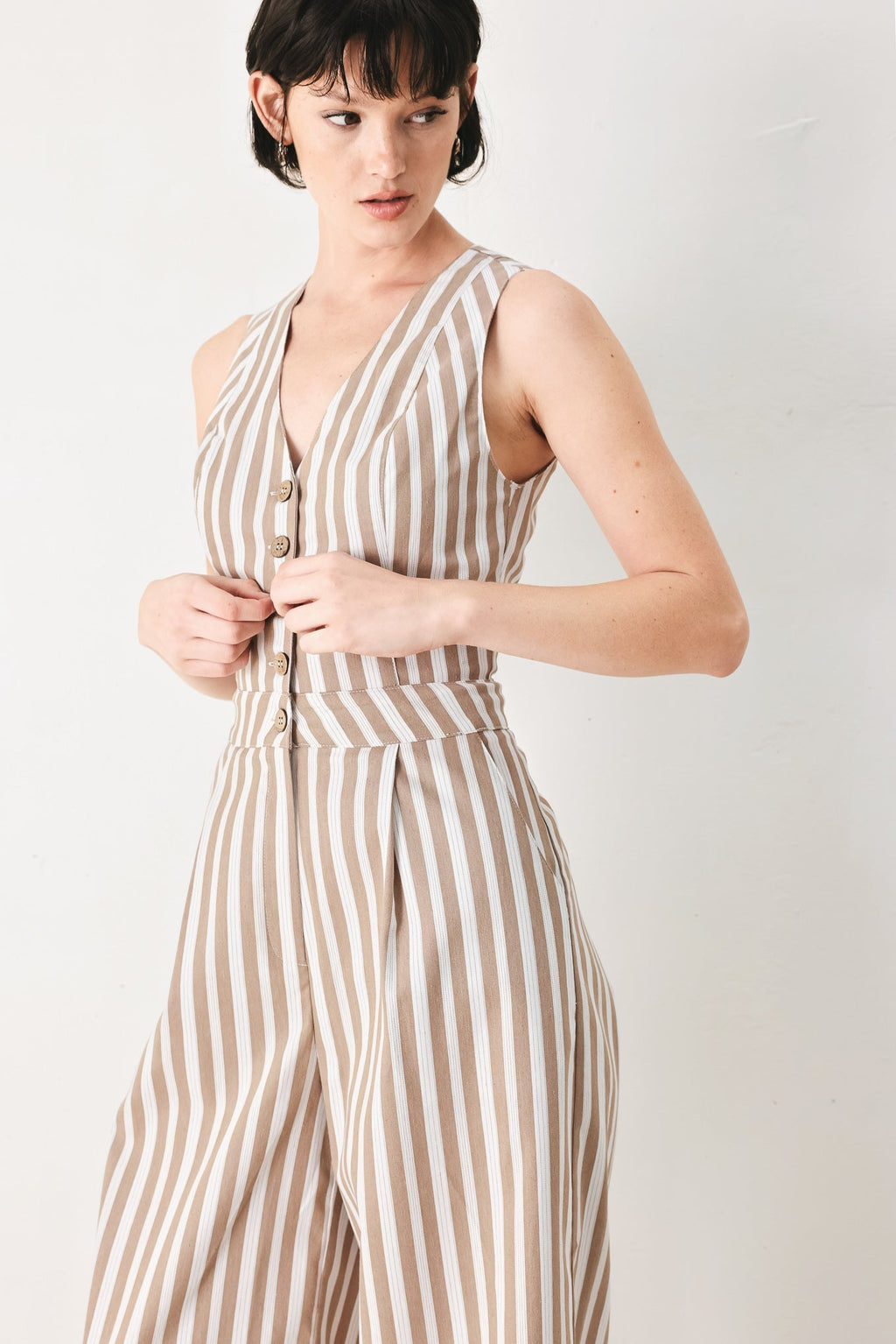 Natural Rhythm Woven Jumpsuit in Taupe White with stripe print, V-neckline, sleeveless cut, front button closure, and wide leg shown on model