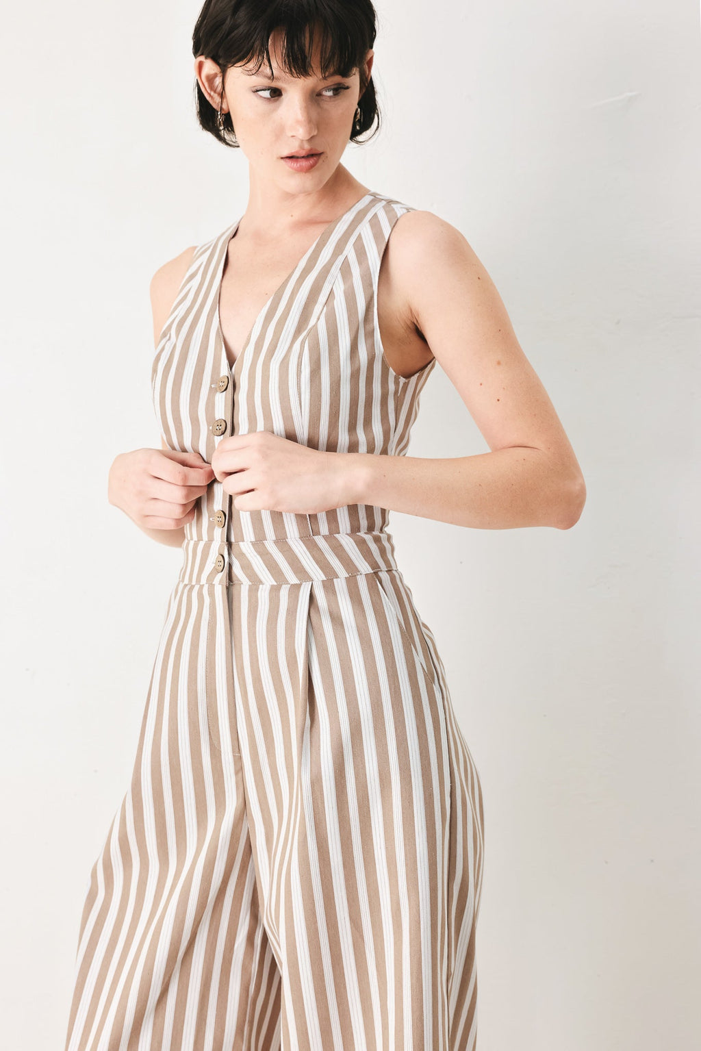 Natural Rhythm Woven Jumpsuit in Taupe White with stripe print, V-neckline, sleeveless cut, front button closure, and wide leg shown on model