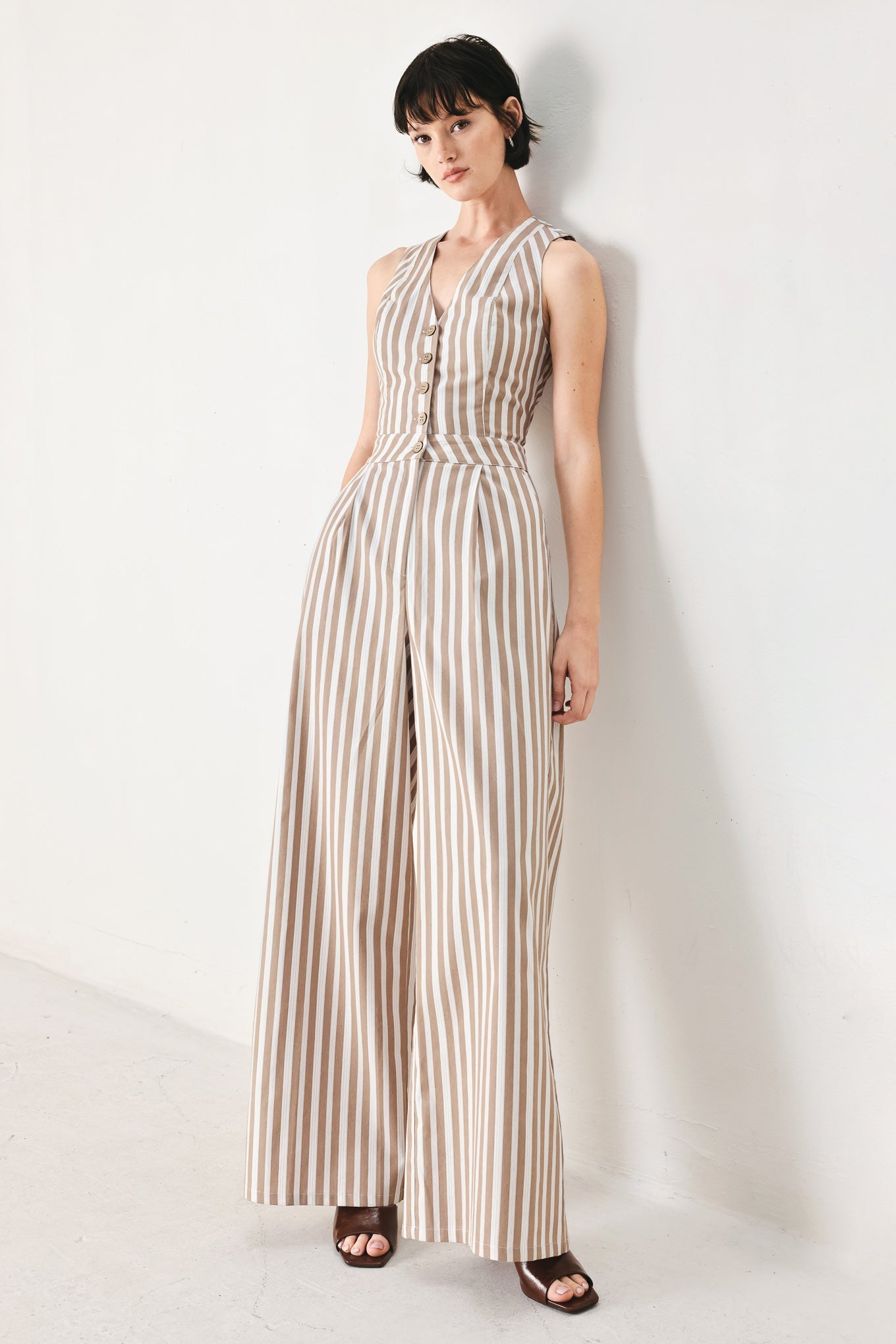 Natural Rhythm Woven Jumpsuit in Taupe White with stripe print, V-neckline, sleeveless cut, front button closure, and wide leg shown on model