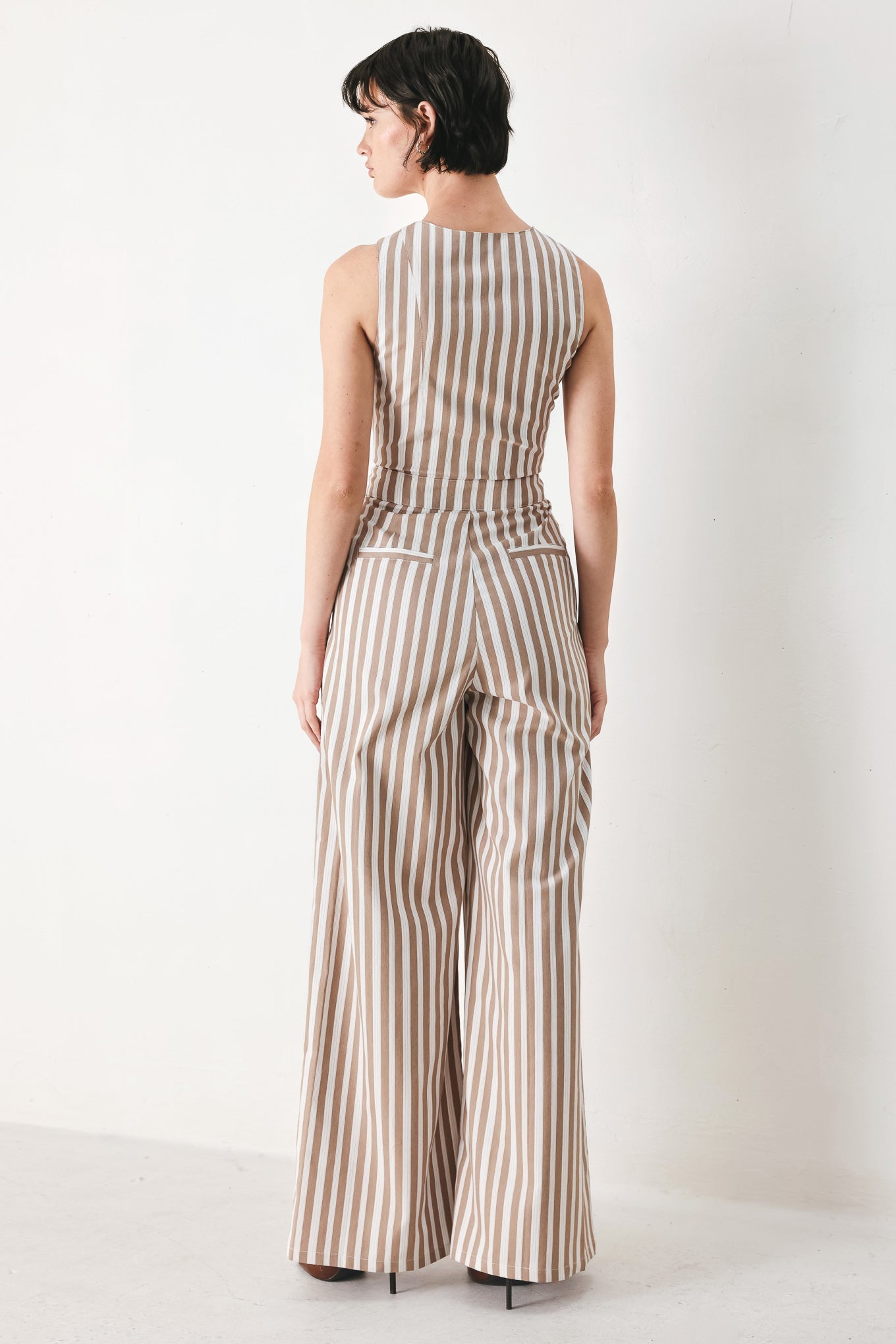 Natural Rhythm Woven Jumpsuit in Taupe White with stripe print, V-neckline, sleeveless cut, front button closure, and wide leg shown on model