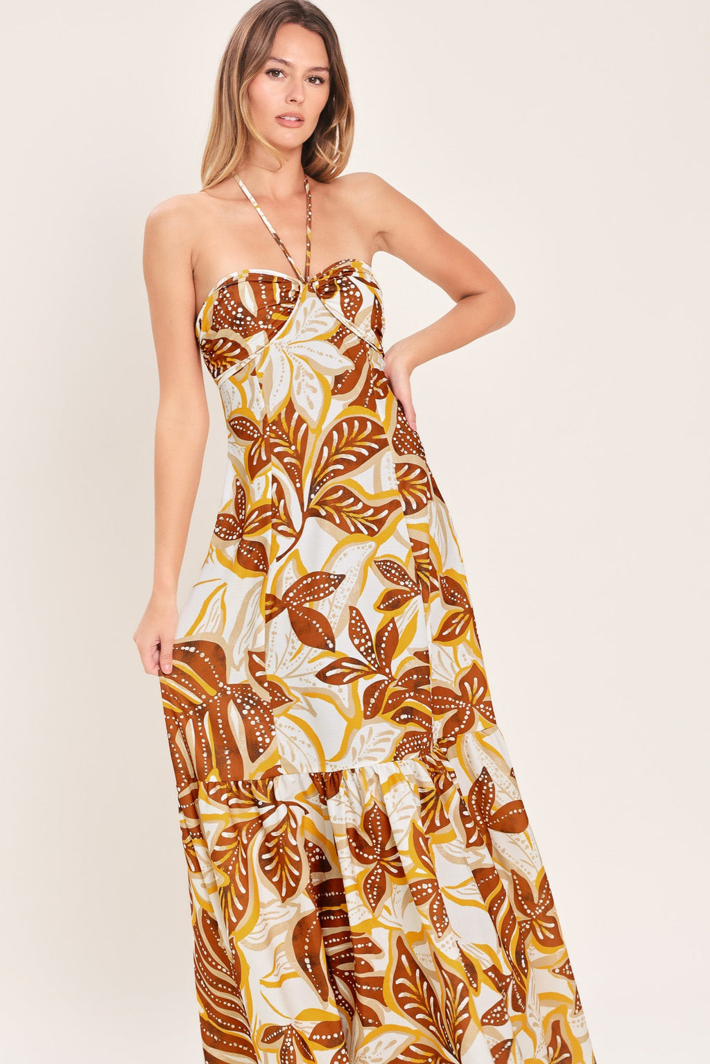 Amber Palm Paradise Woven Maxi Dress in Mustard Brown with palm print, halter tie neckline, ruffle hem, and back zipper closure shown on model