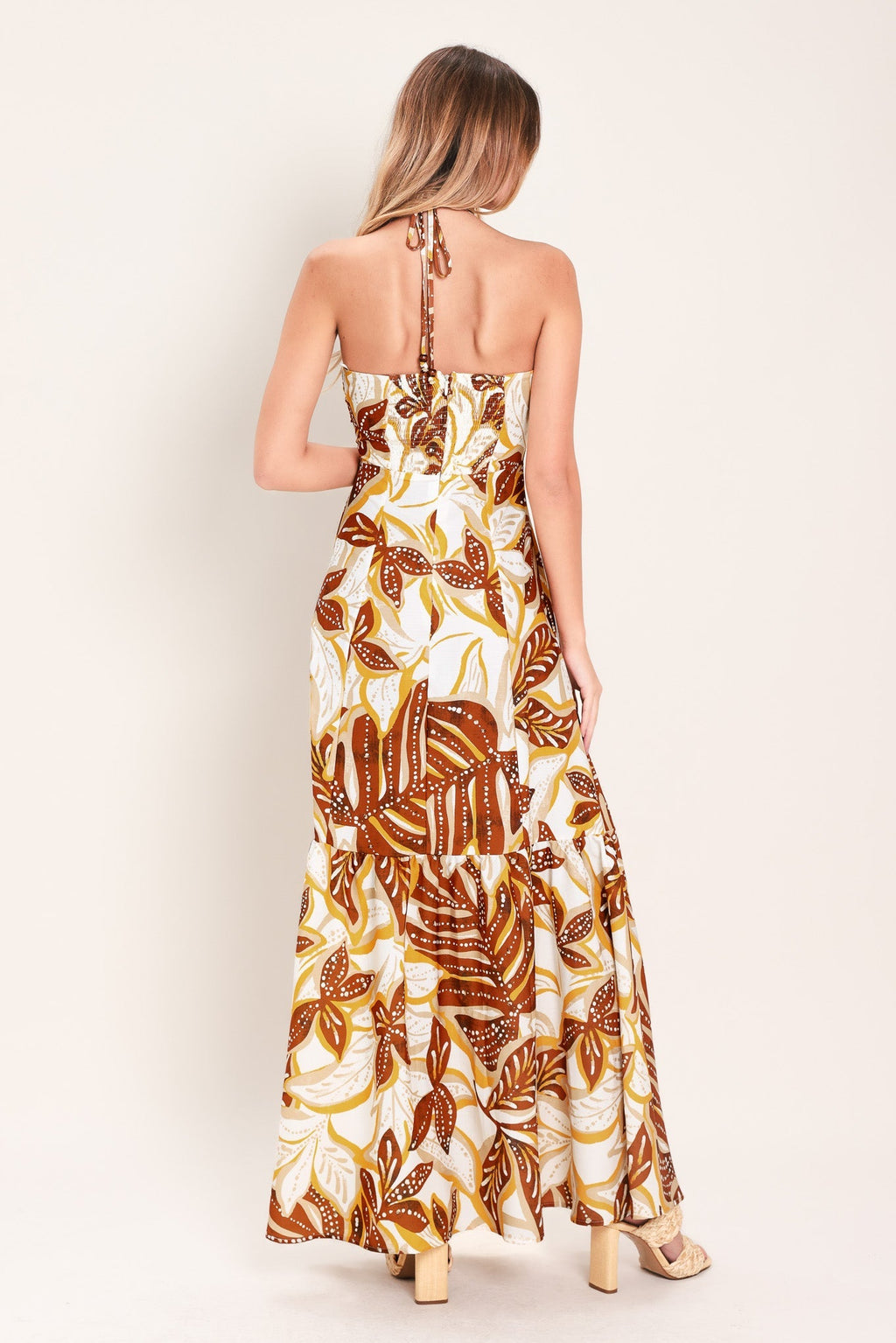 Amber Palm Paradise Woven Maxi Dress in Mustard Brown with palm print, halter tie neckline, ruffle hem, and back zipper closure shown on model